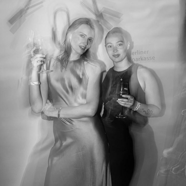 Eventfotografie Zwei junge Frauen posieren mit einem Martini-Glas in den Händen vor einer Wand