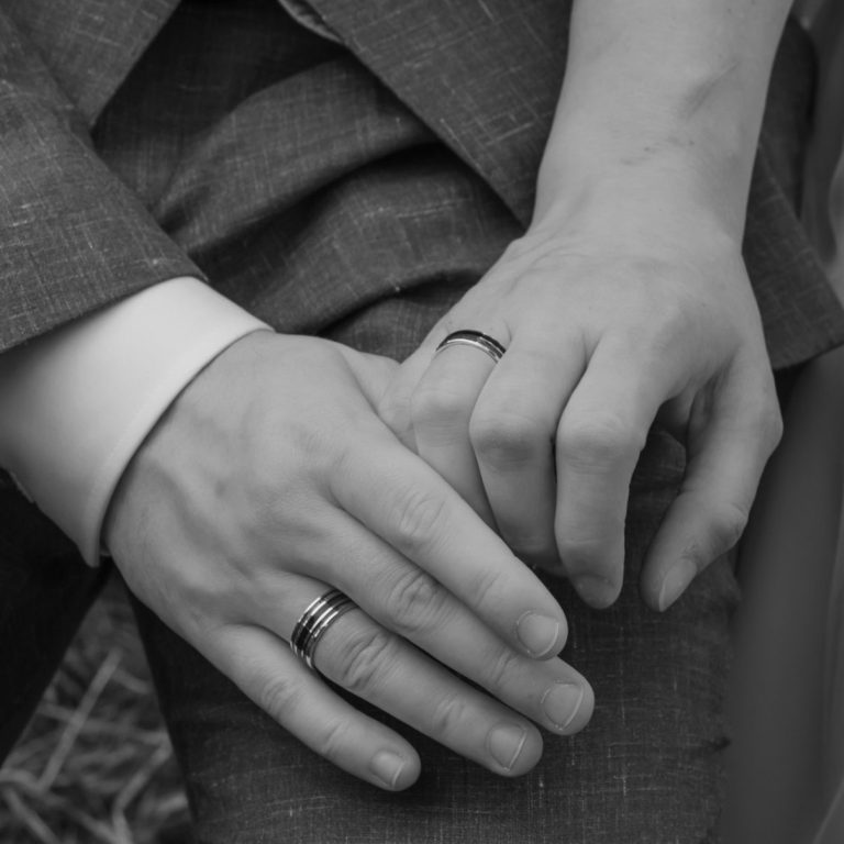 Hochzeitsfotografie Ein Ehepaar steckt sich gegenseitig vor dem Brustkorb der Frau die Ringe an.